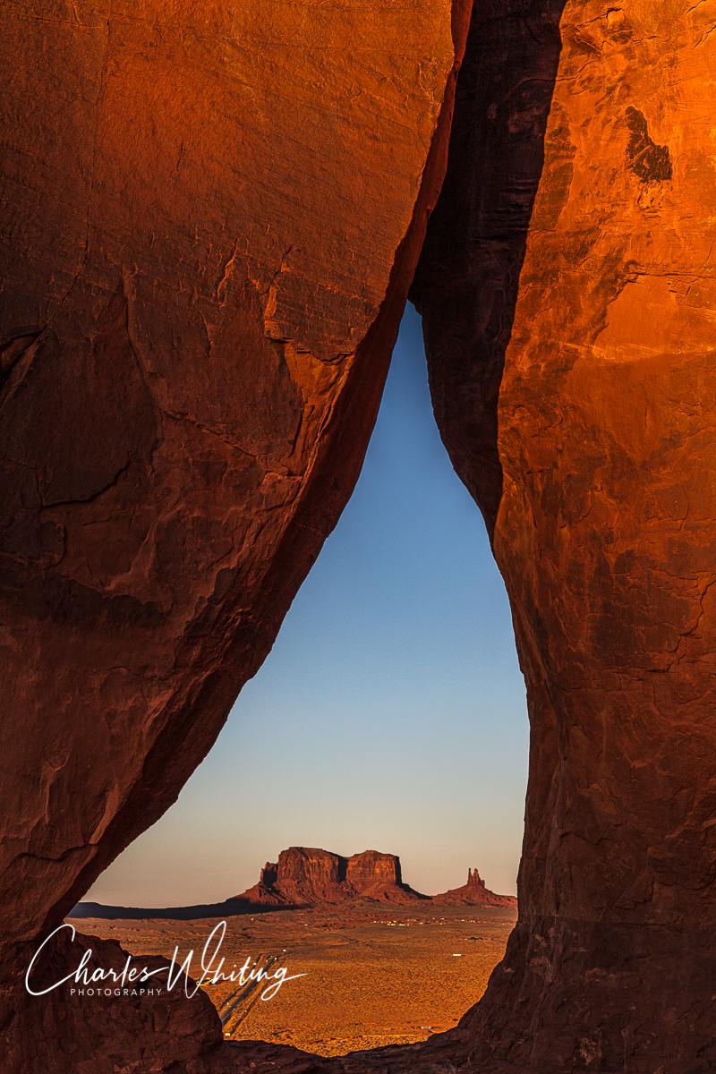 A sunset imaget of a distant butte and Yei bi chei through Teardrop Arch